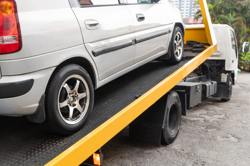 Broken down car being towed onto flatbed tow truck with cable for repair at workshop garage
