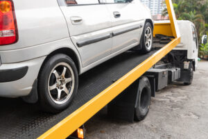 Broken down car being towed onto flatbed tow truck with cable for repair at workshop garage