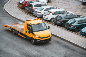 A front view of an orange tow truck with a flatbed and a winch on a city street. Tow truck is about to help a broken car that needs emergency assistance. the service and transportation in the urban