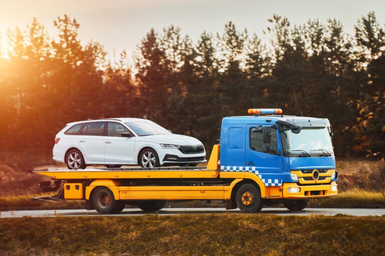 A tow truck carries a broken car on the highway in bad weather. Roadside assistance helps a driver in trouble. Rollback tow truck.